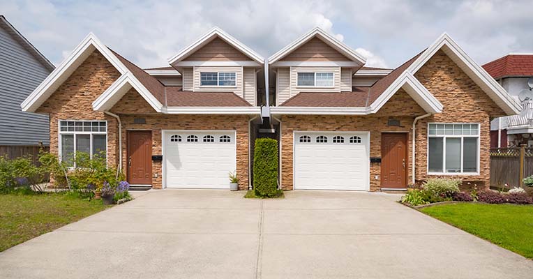 Residential duplex house with concrete drive way and green lawns in front. Two family dwelling with green lawn in front